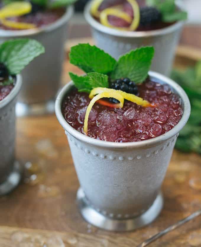 A silver metal cup with blackberry-lemon mint julep.  It's garnished with a lemon peel and fresh mint leaves