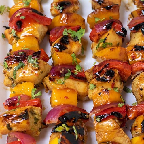 Wooden skewers of chicken, red bell pepper, red onion and mango. They're slightly blackened from being grilled and they have a sweet chili glaze on them with a sprinkle of fresh cilantro.