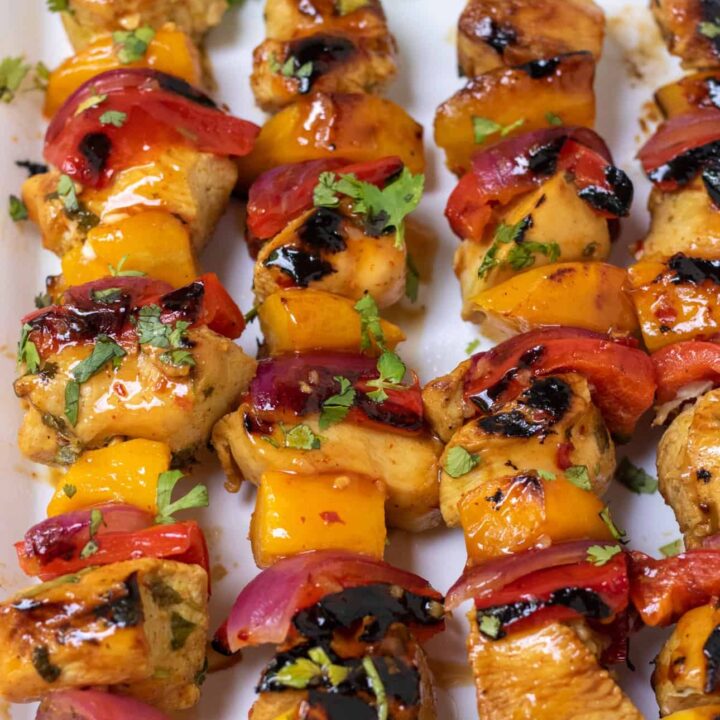 Wooden skewers of chicken, red bell pepper, red onion and mango. They're slightly blackened from being grilled and they have a sweet chili glaze on them with a sprinkle of fresh cilantro.