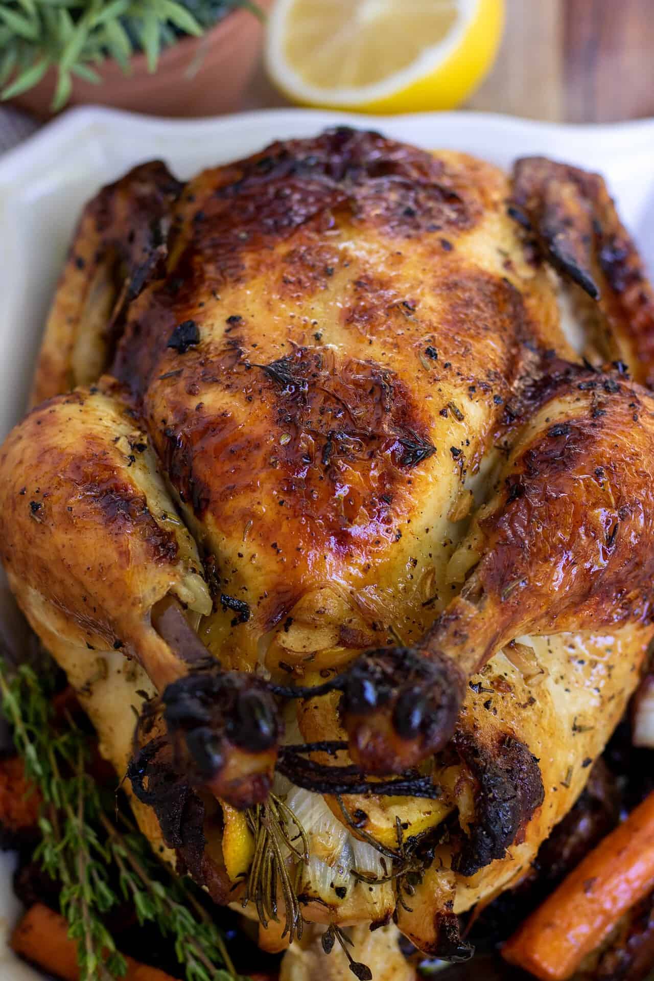 A whole chicken that's been roasted until golden and browned. The skin looks crispy and browned. There's fresh sage and a half of a lemon in the background.