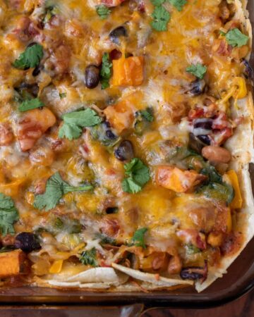 A glass baking dish with enchilada casserole. It's topped with fresh cilantro. You can see the colorful veggies in the casserole