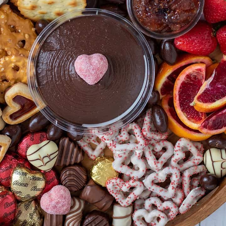 A charcuterie board for valentine's day with chocolates, strawberries, prosciutto,candies, pretzels and chocolate hummus in the middle.