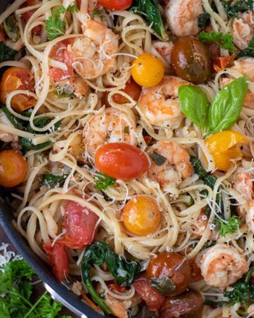 A large saute pan filled with pasta, tomatoes, shrimp and spinach. It's garnished with fresh basil and grated cheese