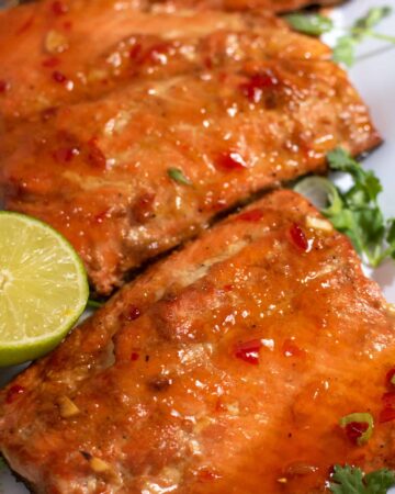 A close up of air fryer salmon that's been brushed with a sweet chili glaze. There's cilantro and a half of lime next to it.
