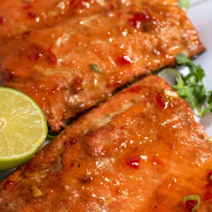 A close up of air fryer salmon that's been brushed with a sweet chili glaze. There's cilantro and a half of lime next to it.