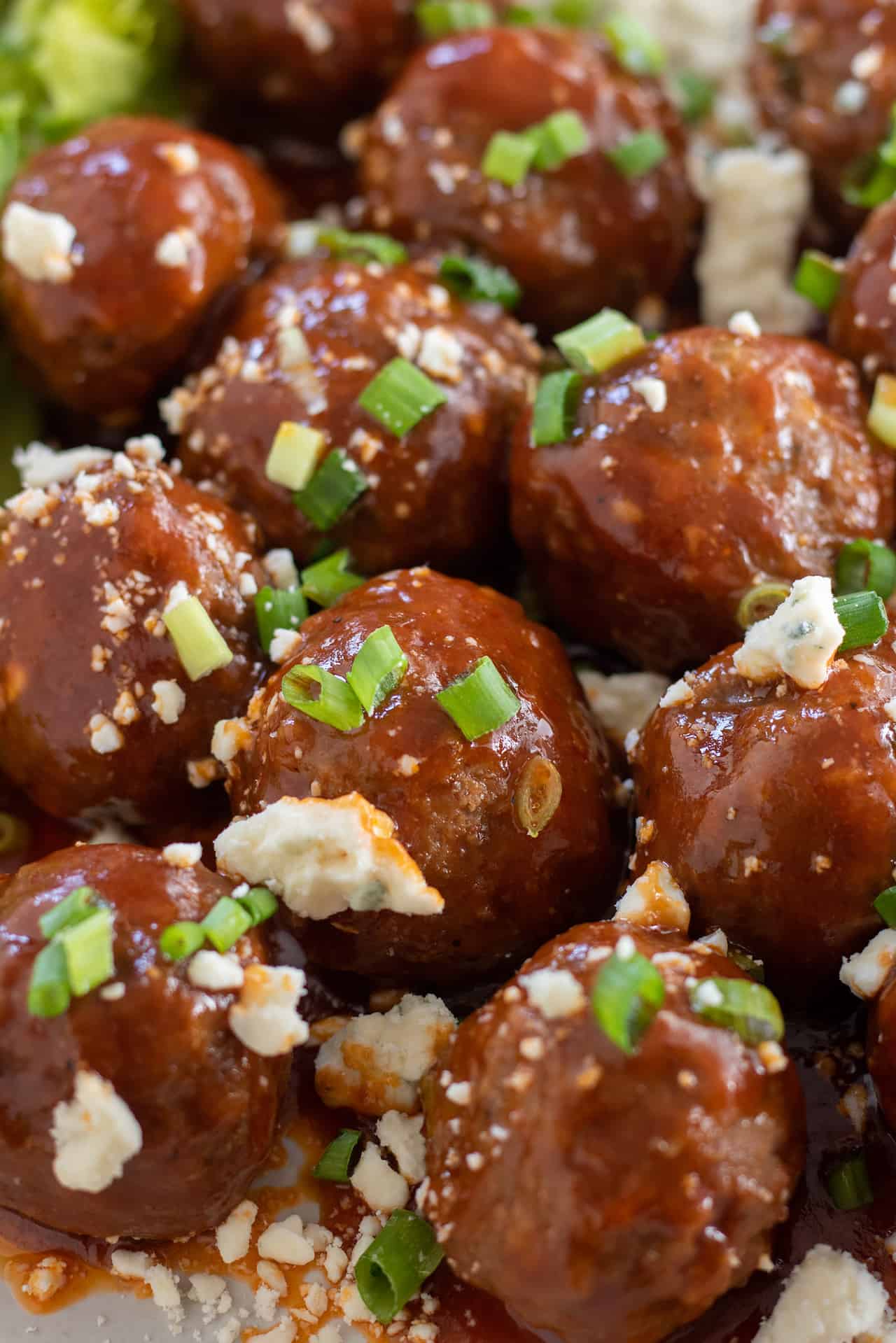A close up shot of chicken meatballs with buffalo bbq sauce smothered on them. They're topped with blue cheese and chopped green onions