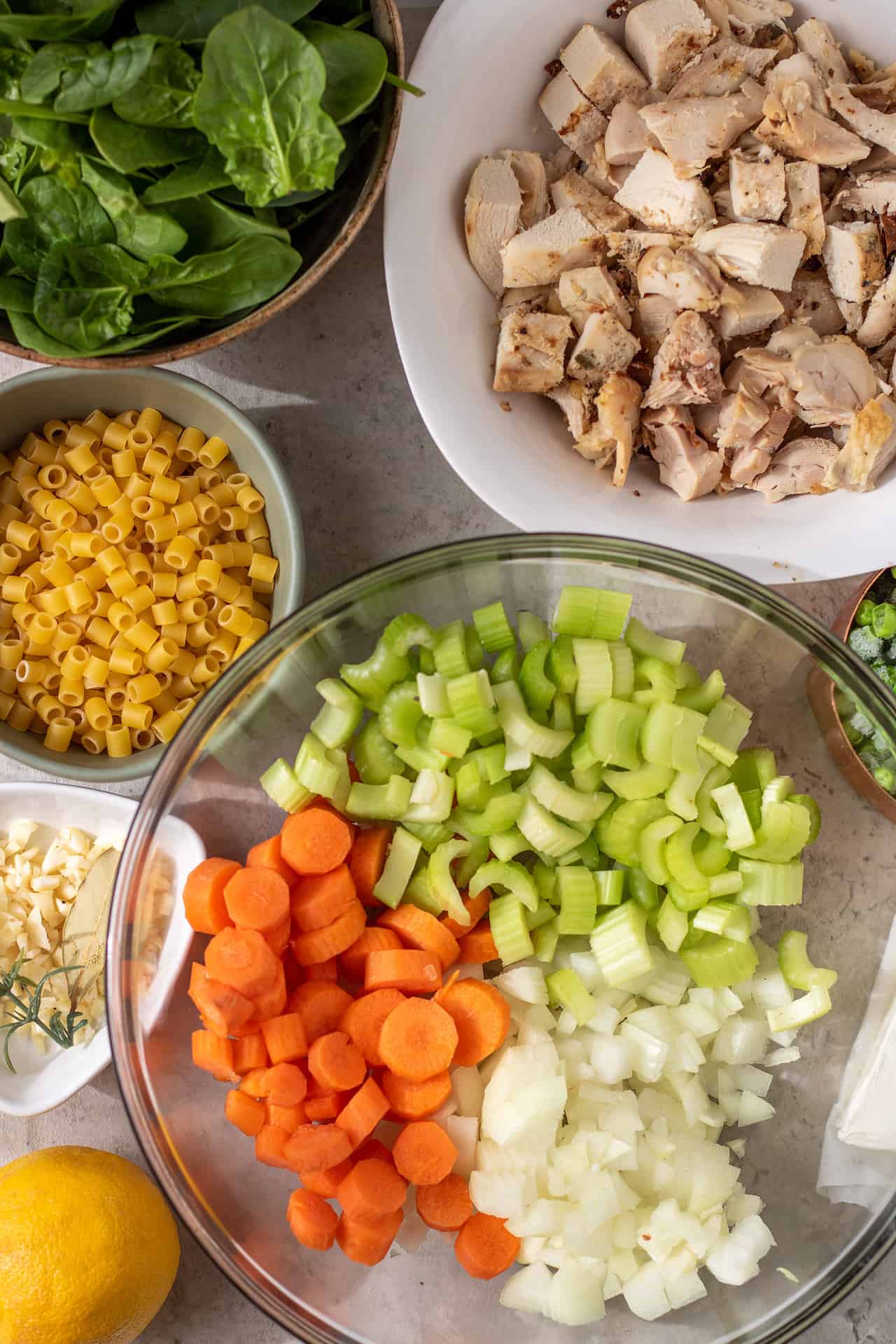 Ingredients for instant pot creamy chicken soup. A big bowl with chopped onions, celery and carrot. A bowl of fresh spinach, a bowl of pasta and a bowl of cooked rotisserie chicken