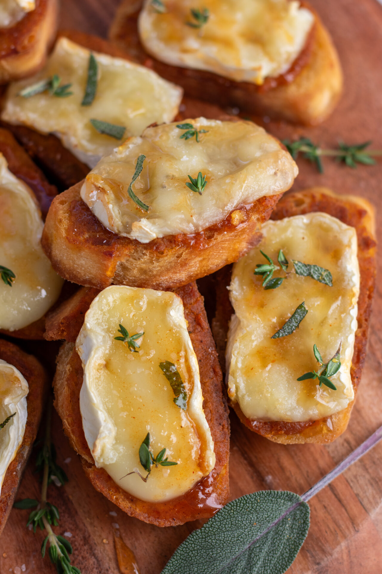 Baked brie crostini topped with fresh thyme and sage and drizzled with hot honey. It's made with pumpkin butter.